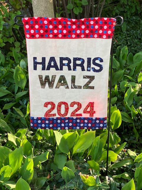 Homemade garden flag, ivory background, red/white and blue border, surrounded by greenery; HARRIS WALZ 2024