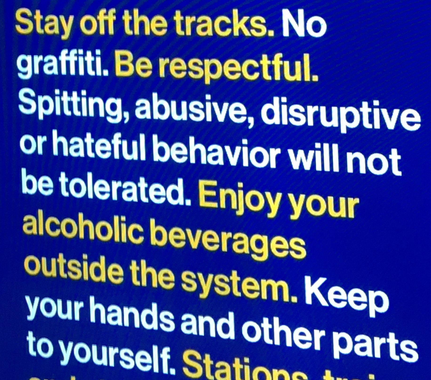 Photo of NYC subway rules, "stay off tracks. No graffitti. Be respectful. Spitting, abusive, disruptive or hateful behavior will not be tolerated..." Blue background, yellow and white text