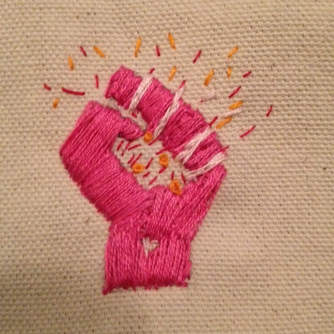 a fuschia-pink woman's fist, sparks in her palm and escaping her grasp, hand embroidered on ecru canvas