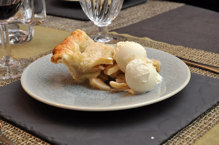 Apple pie with Vanilla ice cream, on a grey-on-grey place setting, lattice-woven placemat, glassware in the background