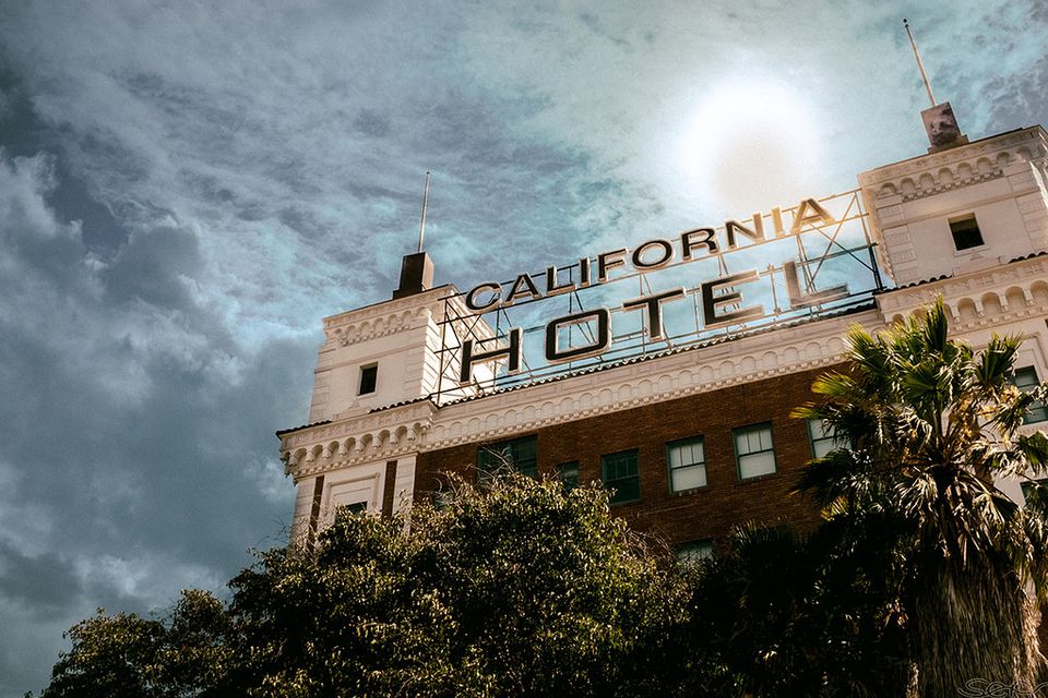 Photo of hotel in daylight, neon sign "California Hotel," noirish vibe.