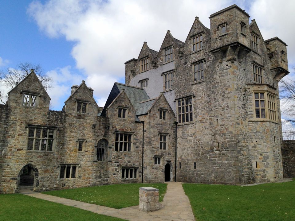Donegal Castle, a stone castle on a green lawn, on a bright, partly-cloudy day