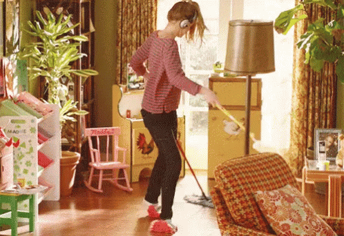 Woman cleaning house by sliding on rags, while also using a dustmop and feather duster
