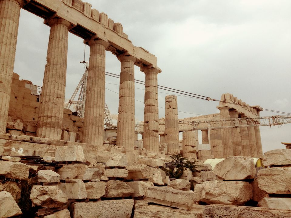 Acropolis, golden and rust colored stone against a grey cloudy sky, showing the cables that are propping up the structure