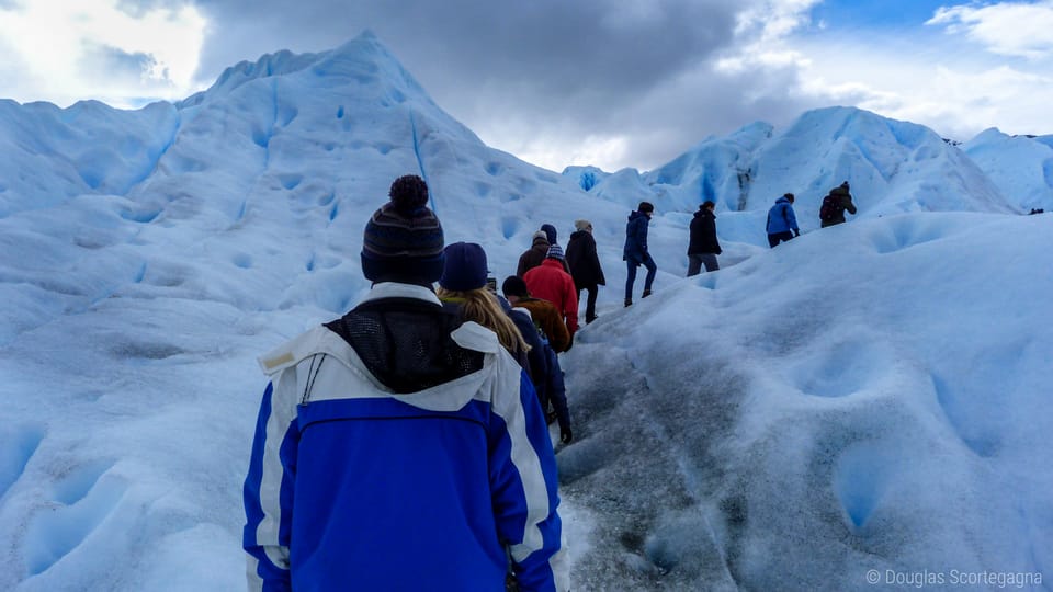 12 people ice trekking, Perito Moreno Glacier, El Calafate, Patagonia. Colorful winter clothing, cloudy sky, blue/white ice.